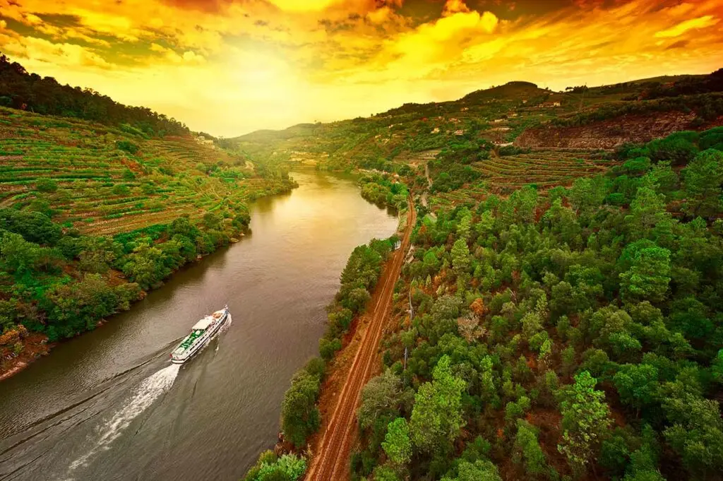 River cruise boat sailing through the scenic Douro Valley vineyards at sunset in Portugal