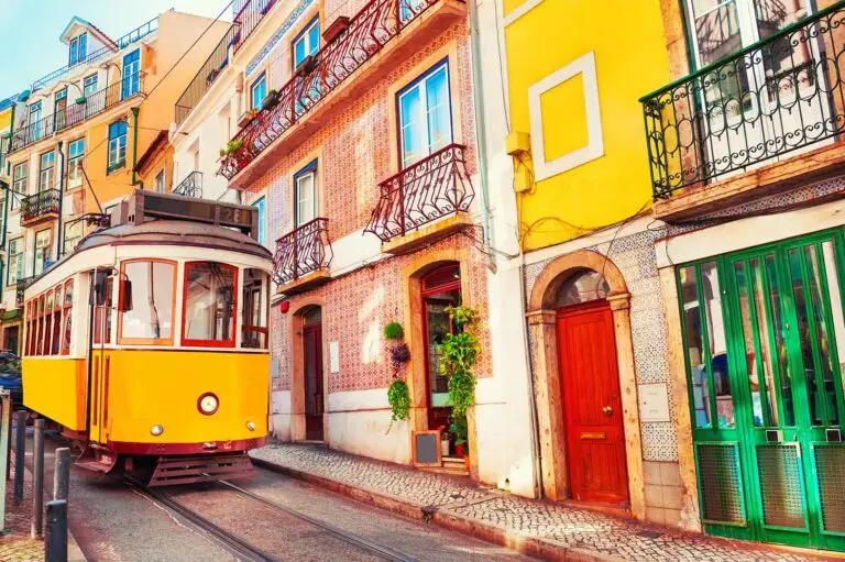 Historic yellow tram passing through colorful old town streets in Lisbon Portugal
