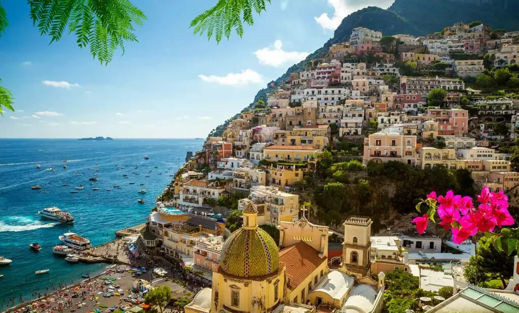 Colorful coastal view of Positano Italy with hillside houses, beach, boats on the Tyrrhenian Sea, and vibrant flowers, a popular travel destination on the Amalfi Coast.