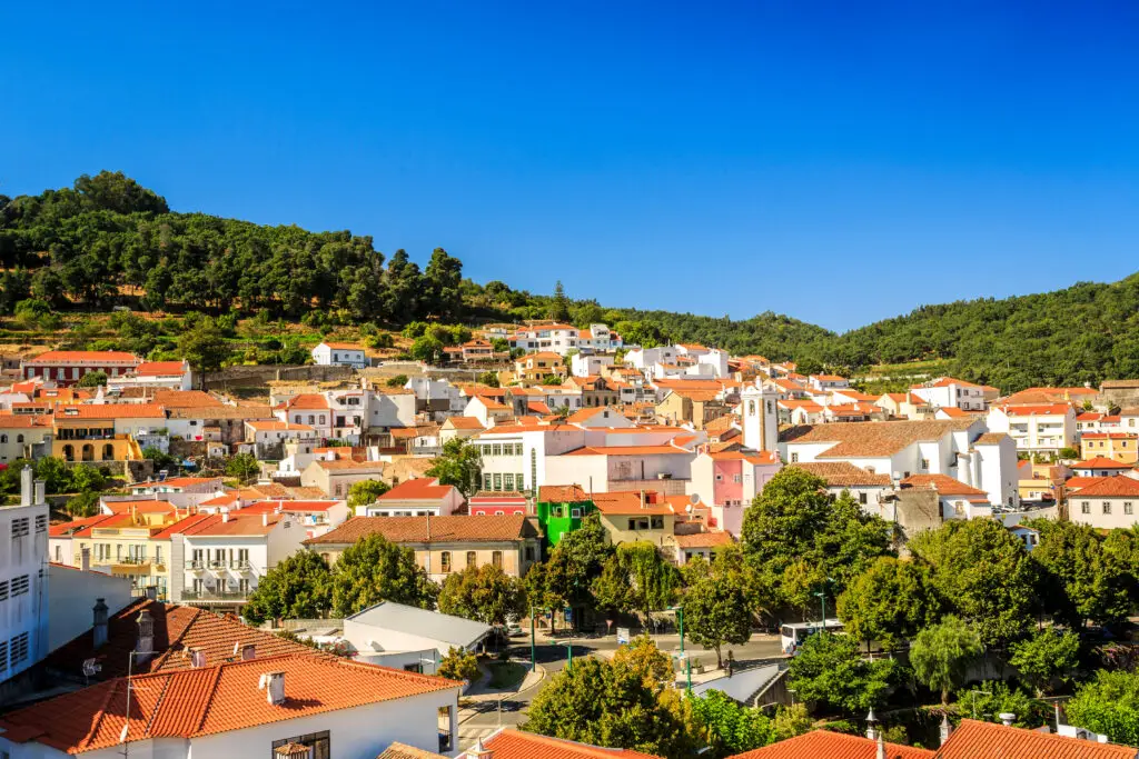 Scenic view of charming Monchique village in the mountains of Algarve, Portugal, with traditional white houses, red tile roofs, and lush green hills under a clear blue sky