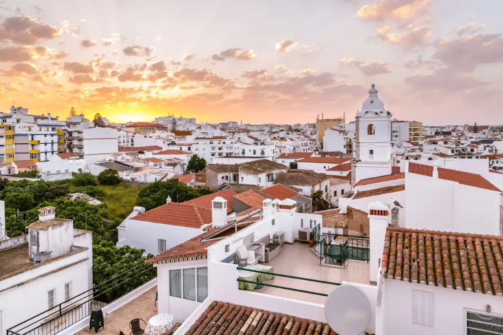 Sunrise over the historic town centre of Lagos in the Algarve, Portugal, featuring traditional whitewashed buildings with terracotta roofs and church tower views