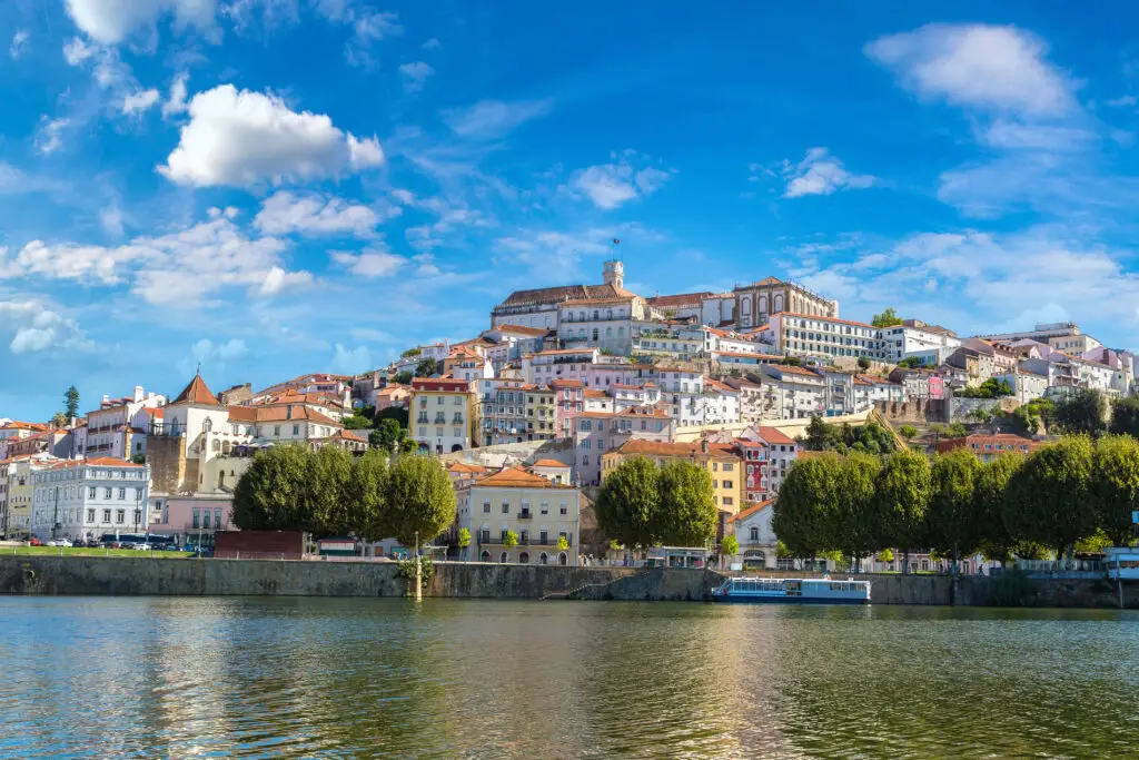 Panoramic view of the old city of Coimbra, Portugal with historic buildings, colorful houses, and the Mondego River under a bright blue sky