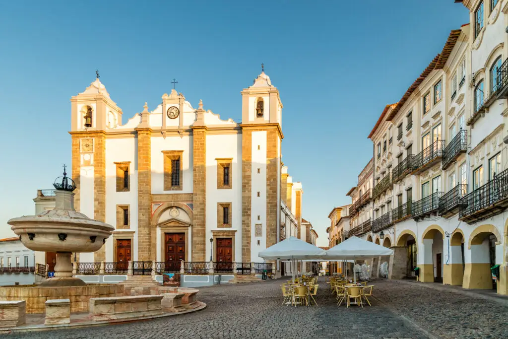 Giraldo Square and Antao Church in Evora Portugal with historic architecture fountain and outdoor café tables at sunset