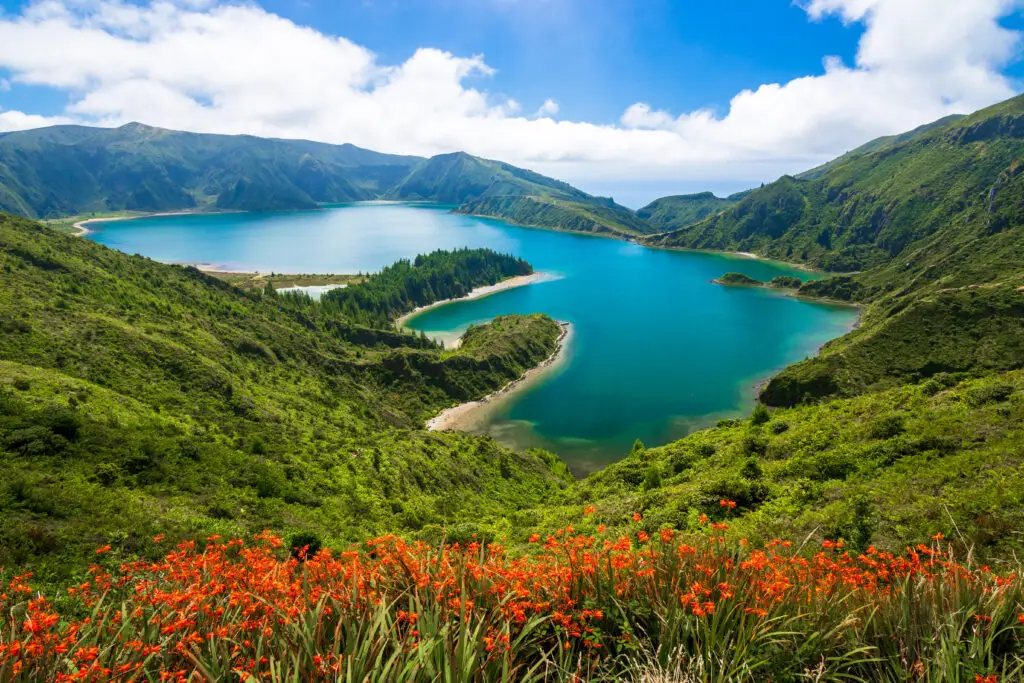 Panoramic view of Lagoa do Fogo lagoon surrounded by lush green mountains and wildflowers on São Miguel Island in the Azores, Portugal