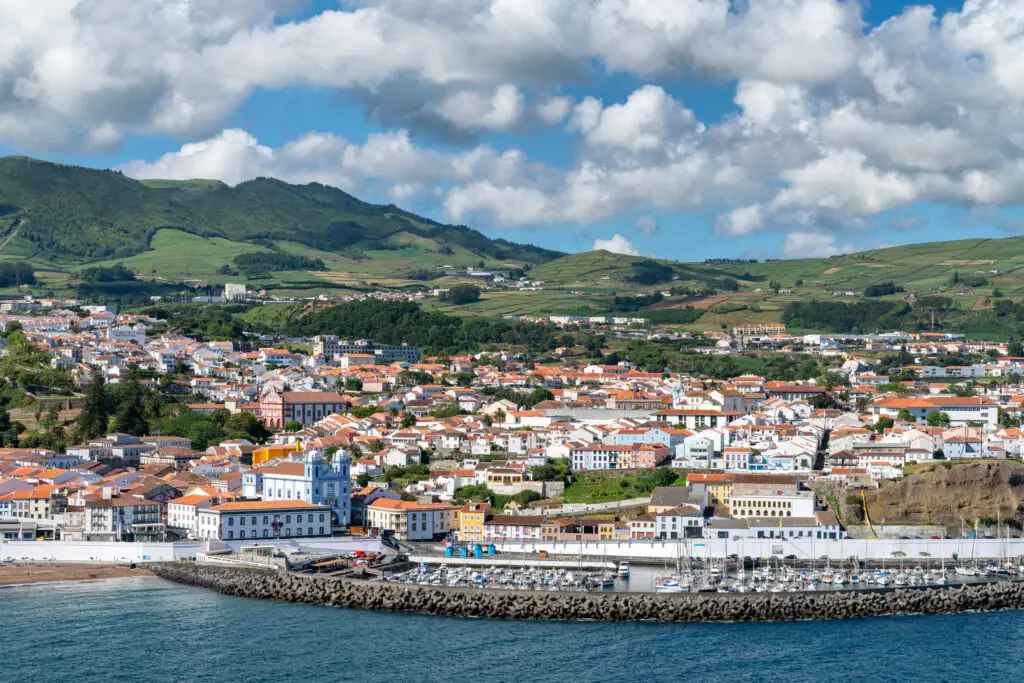 Panoramic view of Angra do Heroísmo town on Terceira Island, Azores, Portugal with colorful historic buildings, marina, and lush green hills in the background