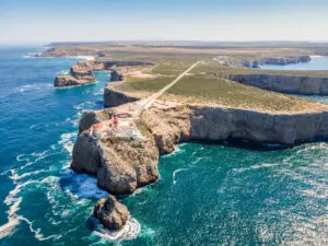 Aerial view of the Saint Vincent Cape lighthouse perched on dramatic cliffs overlooking the Atlantic Ocean in Algarve, Portugal, a popular tourist destination for scenic coastal tours