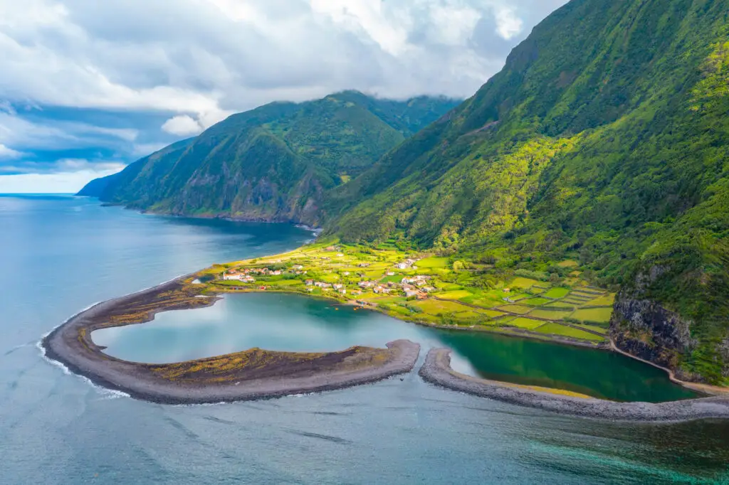 Aerial view of Fajã da Caldeira de Santo Cristo on São Jorge Island in the Azores, Portugal, showing the coastal lagoon, green cliffs, and small village surrounded by lush nature.
