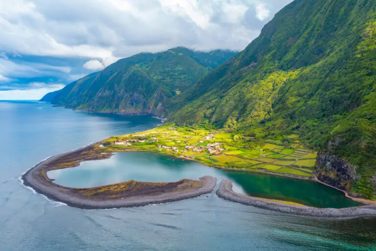 Aerial view of Fajã da Caldeira de Santo Cristo on São Jorge Island in the Azores, Portugal, showing the coastal lagoon, green cliffs, and small village surrounded by lush nature.