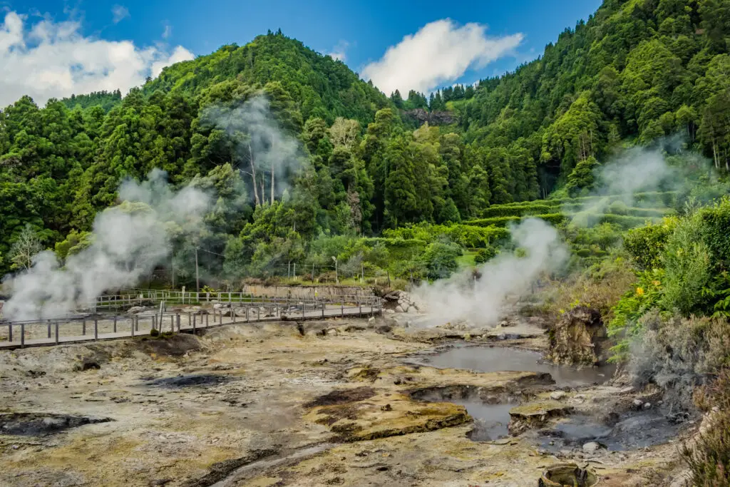 Steaming geothermal hot springs surrounded by lush green forest and mountains in Furnas, São Miguel, Azores, Portugal