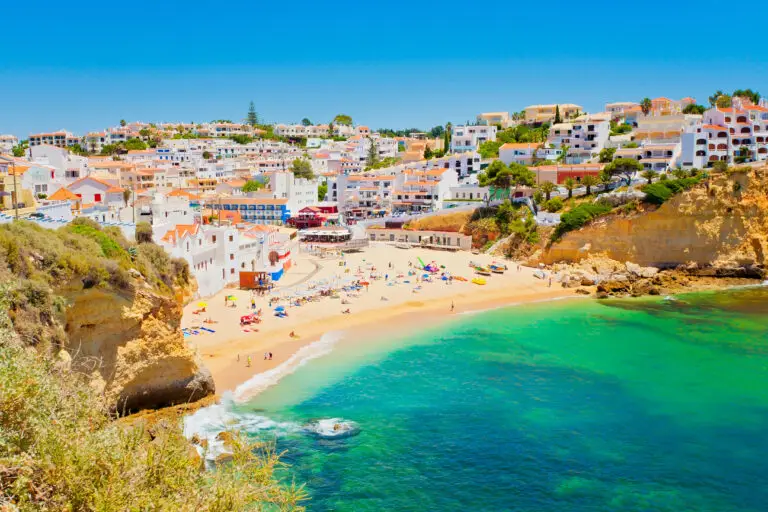 Colorful seaside village and golden cliffs along the Algarve coast in Portugal with turquoise water and a sandy beach filled with tourists enjoying the sun