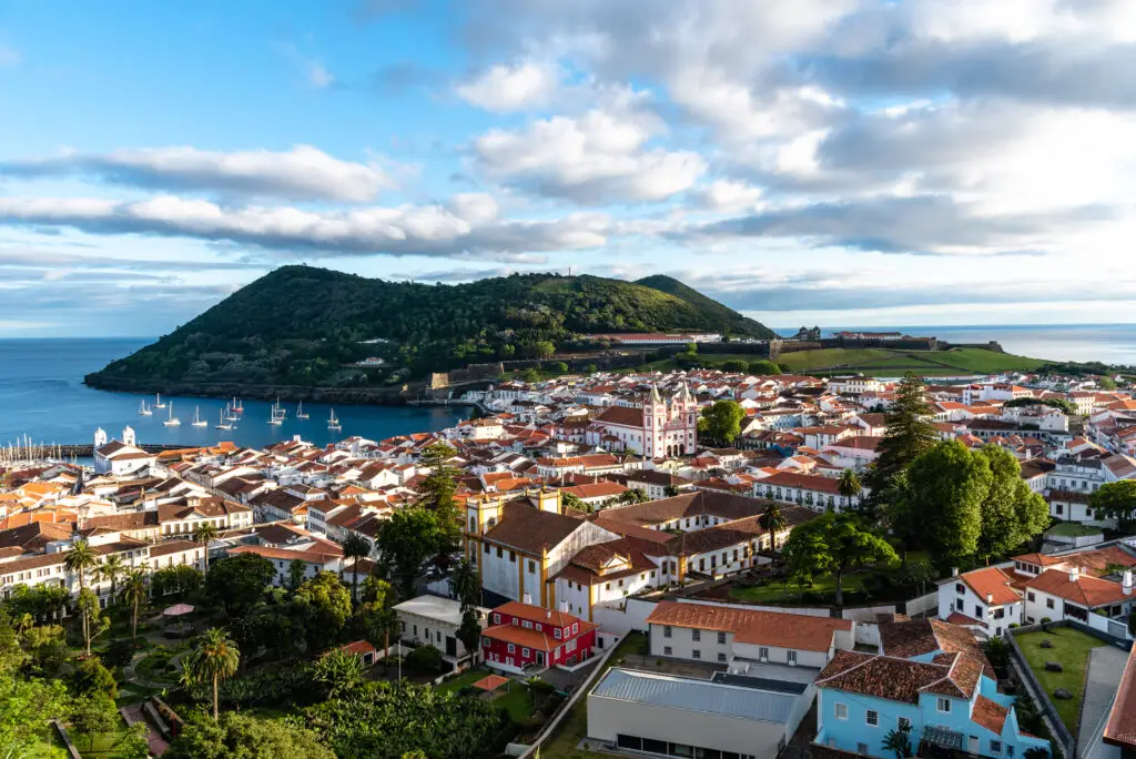 Panoramic aerial view of Angra do Heroísmo old town and harbor on Terceira Island, Azores, Portugal, with colorful buildings, marina, and lush green hills by the Atlantic Ocean