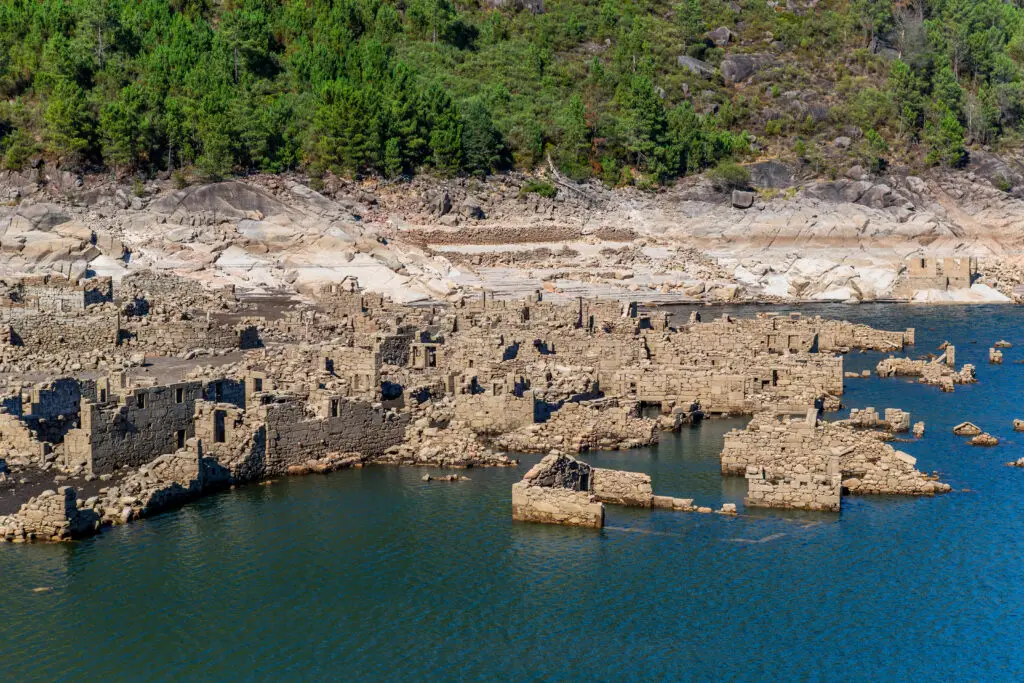 Ancient stone ruins of Vilarinho das Furnas partially submerged in a reservoir surrounded by forested hills in northern Portugal