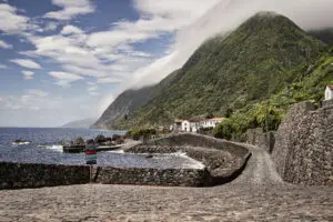 Panoramic view of Fajã de São João village with cobblestone road, ocean, and lush green mountains on São Jorge Island in the Azores, Portugal