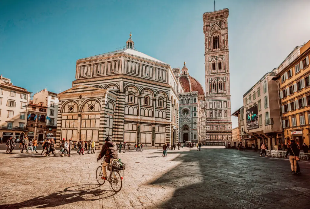 Tourists exploring Piazza del Duomo in Florence Italy with view of the Florence Cathedral Baptistery and Giotto’s Bell Tower on a sunny day