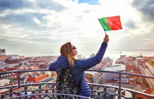 Young woman tourist holding Portuguese flag enjoying panoramic view of Lisbon old town and Tagus River on a sunny day in Portugal