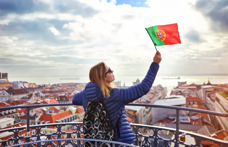 Young woman tourist holding Portuguese flag enjoying panoramic view of Lisbon old town and Tagus River on a sunny day in Portugal