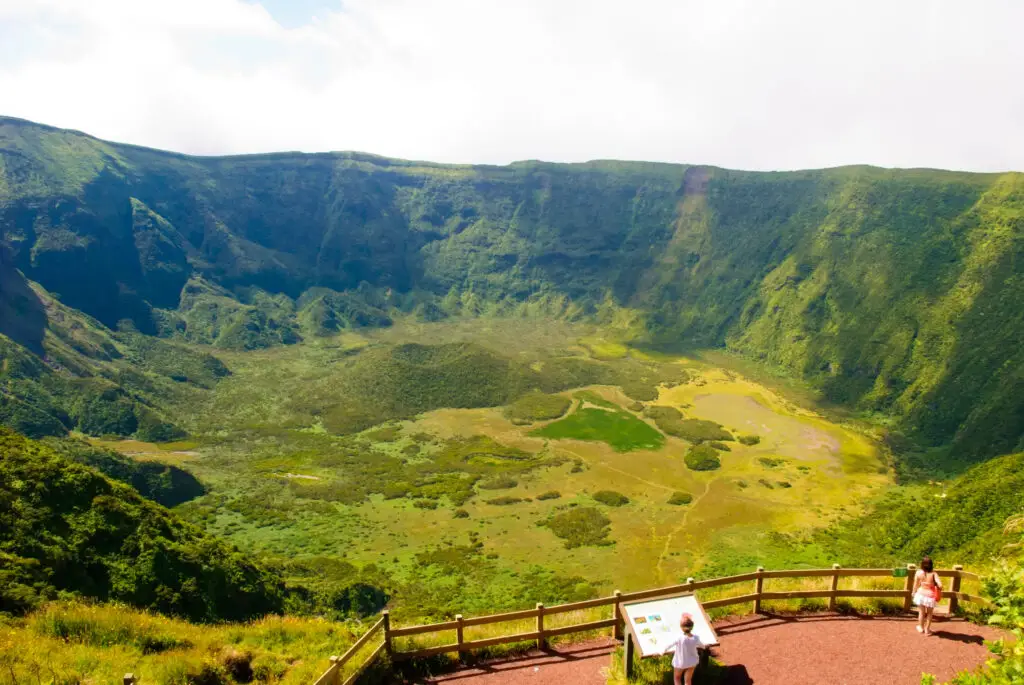 Panoramic view of Caldeira do Faial volcanic crater on Faial Island in the Azores, Portugal, with lush green landscape and visitors enjoying the scenic lookout point.