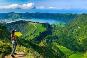 Tourist admiring the stunning landscape of Sete Cidades twin lakes on São Miguel Island in the Azores, Portugal, with lush green hills and crater lake views.