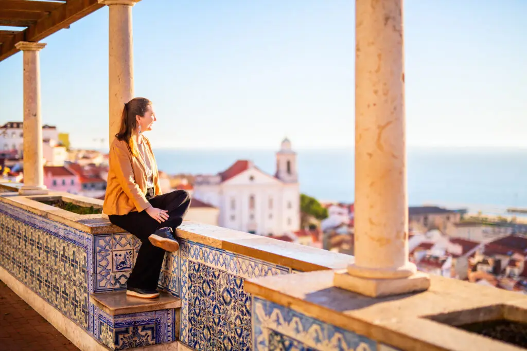 Teenage girl enjoying panoramic view of Lisbon Portugal from a scenic viewpoint with traditional azulejo tiles and ocean in the background