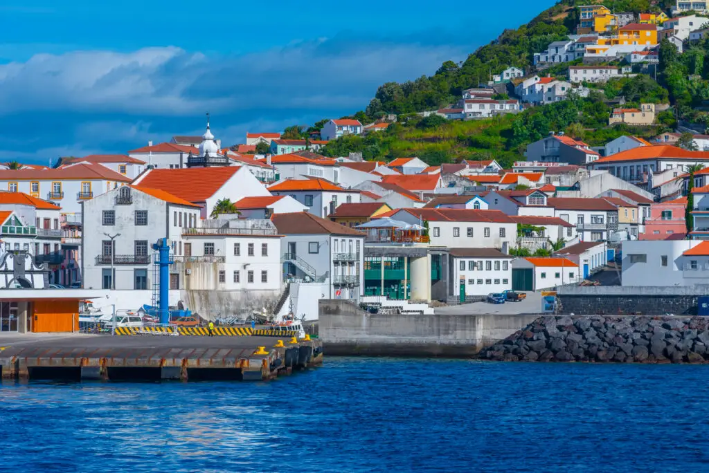 Colorful coastal town and marina at Velas port on São Jorge Island in the Azores, Portugal, with traditional white houses, red-tiled roofs, and lush hillside scenery overlooking the Atlantic Ocean