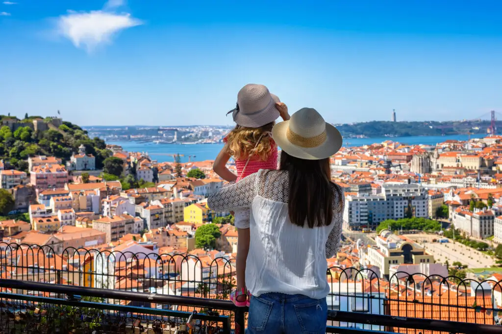 Tourist mother and daughter enjoying panoramic view of Lisbon cityscape with colorful rooftops and Tagus River, Portugal
