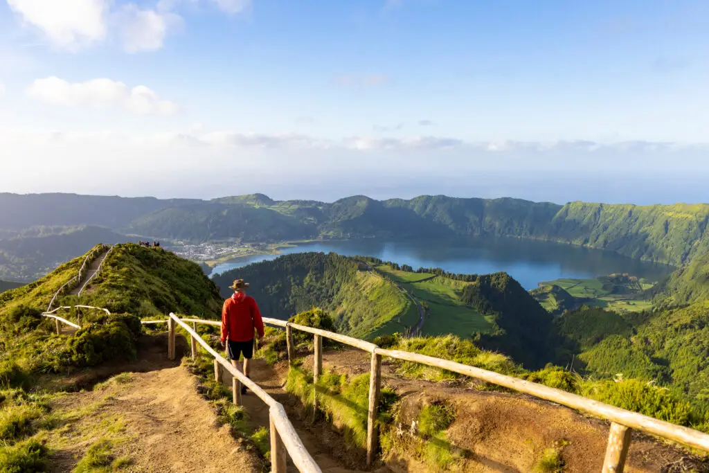 Hiker in a red jacket walking along a scenic trail overlooking the Sete Cidades caldera and lake on São Miguel Island in the Azores, Portugal