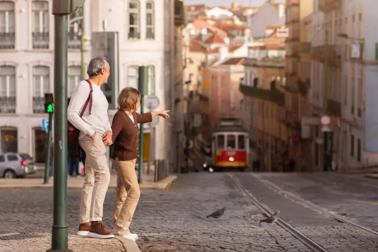 Senior couple sightseeing in Lisbon, Portugal, pointing at the iconic yellow tram on a cobblestone street during a guided city tour