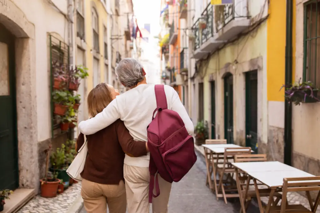 Senior couple walking arm in arm through a charming Lisbon street with outdoor cafes, enjoying a private Portugal tour experience