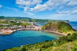 Scenic view of Horta city on Faial Island in the Azores, Portugal, with colorful houses, marina, green hills, and the Atlantic Ocean under a bright blue sky