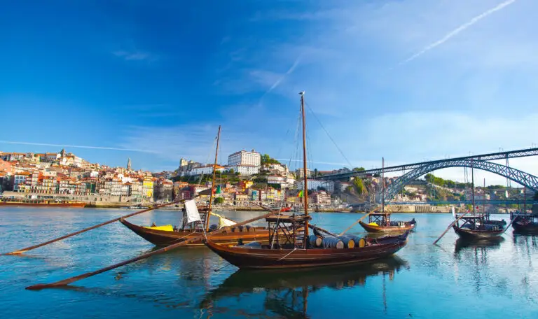 Traditional wooden Rabelo boats on the Douro River in Porto, Portugal, used to transport Port wine barrels, with colorful Ribeira houses and Dom Luís I Bridge in the background