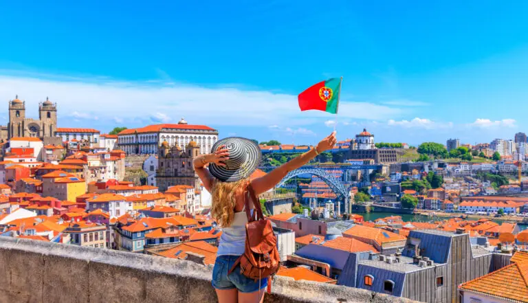 Woman tourist holding Portuguese flag overlooking cityscape and Dom Luís I Bridge in Porto Portugal panoramic viewpoint