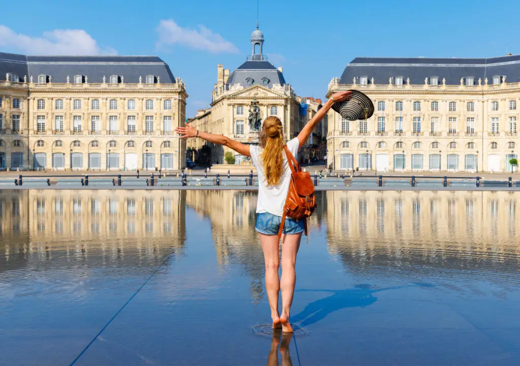 Woman traveler enjoying Place de la Bourse and the Water Mirror in Bordeaux, France during a sightseeing tour in Nouvelle-Aquitaine