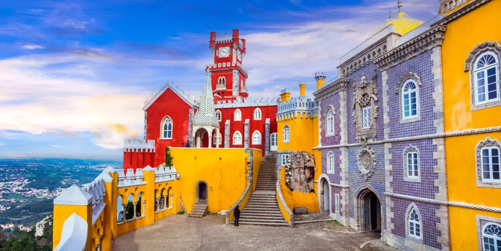 Panoramic view of the colorful courtyard and towers of Pena Palace in Sintra Portugal showcasing vibrant red yellow and blue architecture under a bright sky UNESCO World Heritage Site near Lisbon