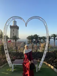 Tourist sitting under a heart-shaped arch with a lighthouse and ocean view in the background during a Private Portugal Tour